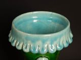 a blue and green vase with a white flower in it