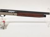 le fusil est posé sur un socle transparent, à côté d'une bouteille de vin