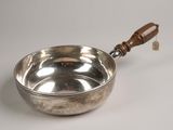 an old silver bowl with a wooden handle on a white surface