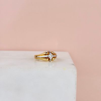 un gros plan d'une bague en or sertie de deux diamants, posée sur un bloc de marbre blanc