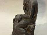 bronze statue of a man sitting on a bench with a crown on his head