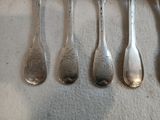 six cuillères en argent sont alignées sur une surface blanche