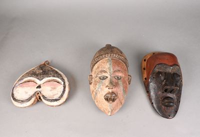 Trois masques en bois sont posés les uns à côté des autres sur une table