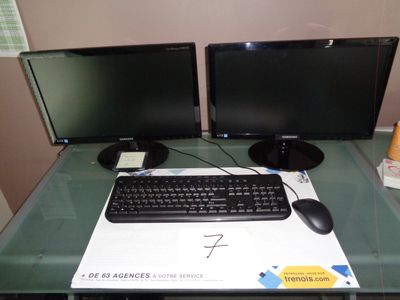 deux écrans d'ordinateur et un clavier posés sur un bureau en verre