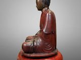 a wooden statue of a buddha sitting on top of a red object