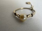 une photo d'une bague sertie d'une perle, posée sur une table