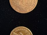 two gold coins sitting on top of a black surface next to each other