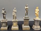 quatre statues en bronze représentant des hommes et des femmes, posées sur des socles disposés sur une table