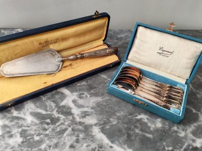 deux pièces d'argenterie dans un coffret bleu posé sur une table