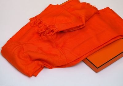 une écharpe orange et une boîte d'oranges posées sur une surface blanche