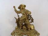a gold clock with a statue of a man with a hat on it