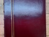 classeur en cuir bordeaux avec des finitions dorées, posé sur un parquet