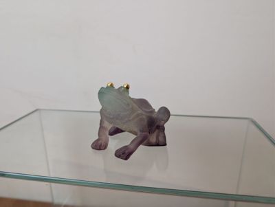 une figurine représentant une grenouille assise sur une table en verre