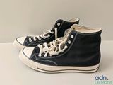 Des baskets Converse noires avec des lacets blancs sont posées sur une surface blanche