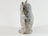 a silver figurine of a cat sitting on a white surface