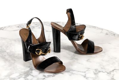 des sandales en cuir noir ornées de boucles dorées, posées sur une table en marbre