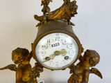 a gold clock with two cherensils on top of it