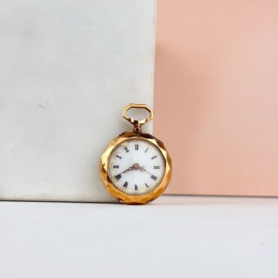montre de poche en or avec des chiffres romains, posée sur un bloc de marbre