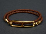 a brown leather bracelet with a gold clasp on a black background