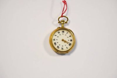 une petite montre de poche en or suspendue à un cordon rouge