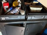 a kitchen with a stove, sink, cabinets, and a trash can