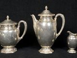 two silver teapots and a sugar bowl on a black background
