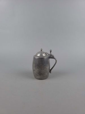 une petite théière en argent munie d'une anse, posée sur une surface blanche