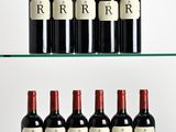 six bottles of red wine are lined up on a glass shelf