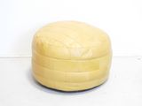 yellow leather pouffe sitting on a white floor in a room