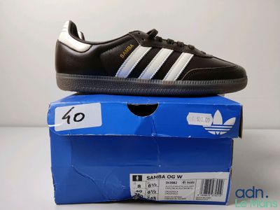 Des chaussures adidas Superstar noires et blanches posées sur une boîte bleue
