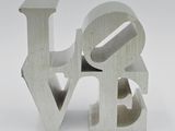 un gros plan d'une sculpture métallique représentant le mot « amour » sur fond blanc