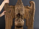 une femme tient dans ses mains une grande sculpture en bois représentant un aigle