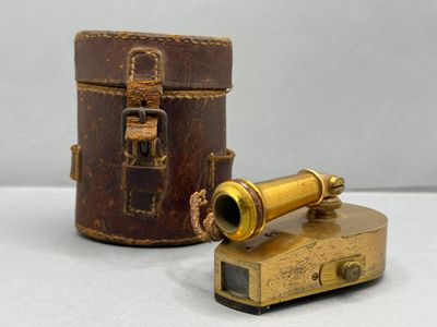 un vieux télescope en laiton dans un étui en cuir, posé sur une surface blanche