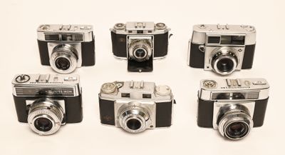 six old cameras are lined up in a row on a white surface