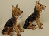 two figurines of dogs sitting next to each other on a white surface