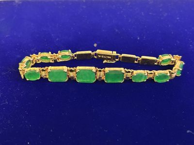 a gold bracelet with green stones on a blue surface