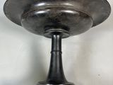 a large metal bowl on a pedestal on a white wall
