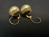 a pair of gold colored pearl earrings on a black surface