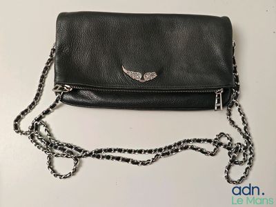 un sac à main en cuir noir orné d'ailes argentées, posé sur une table