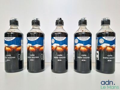 Quatre bouteilles de soda sont posées sur une table devant un fond blanc