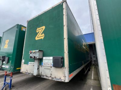 two green semi trucks parked next to each other on the street