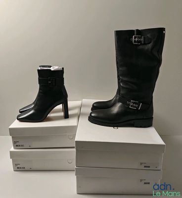 Deux paires de bottes noires sont posées sur une pile de cartons blancs.