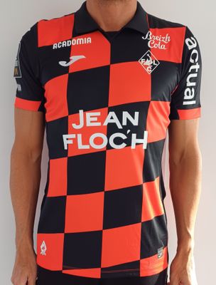 Cet homme porte un t-shirt rouge et noir et un pantalon noir.