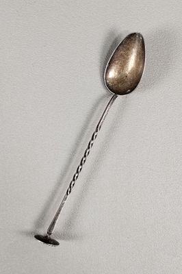 une cuillère en argent à long manche posée sur une surface blanche