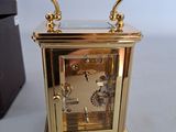 a small gold clock sitting on a table next to a black box