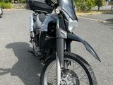 une moto noire garée sur un parking, avec des arbres en arrière-plan