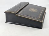 an old black box with gold trim and a lid on a white surface