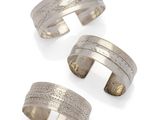 a set of three silver cuff bracelets on a white background