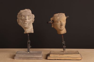two sculptures of heads on a wooden stand on a table