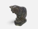 statue of a cat sitting on a rock on a white surface